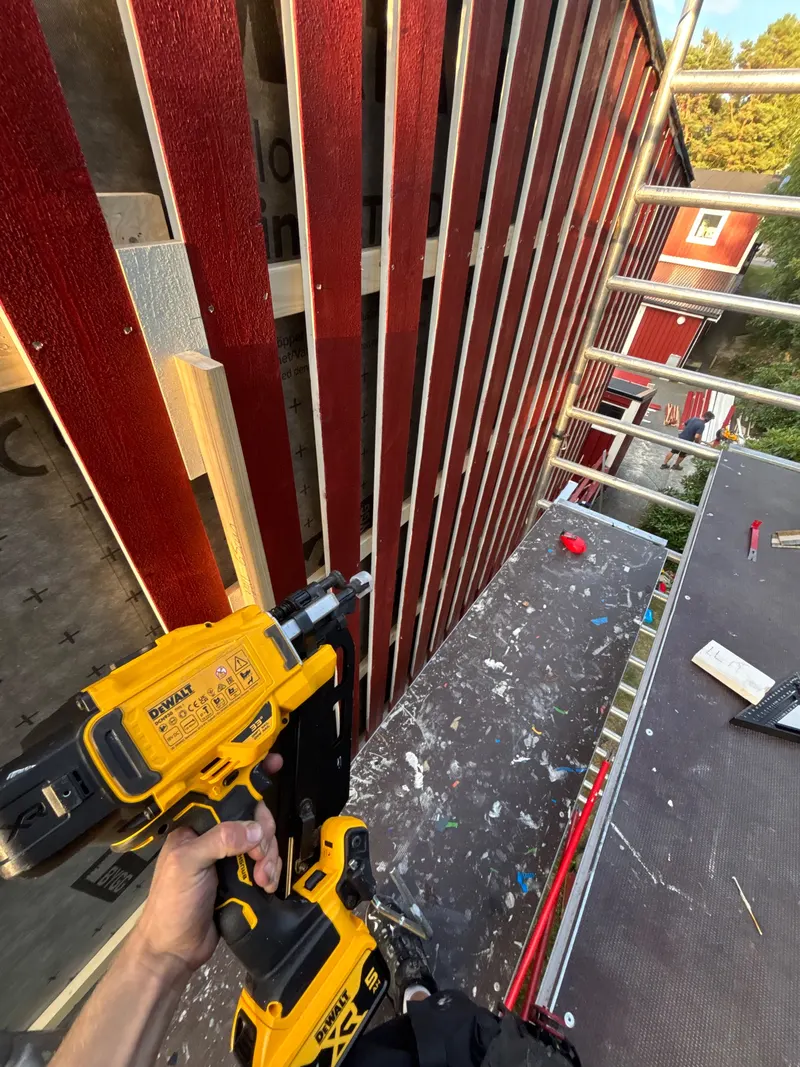 Röd träpanel monteras på fasaden från byggställning